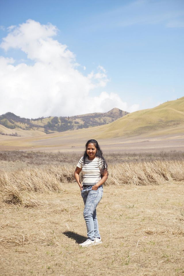 A young girl standing confidently in a scenic outdoor landscape, wearing stylish jeans and a striped shirt