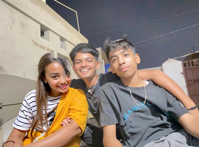 A warm outdoor scene at night featuring a mother and two teenage boys, all smiling and enjoying each other's company