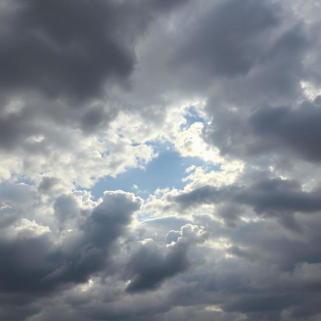 An expansive view of a cloudy sky filled with varying shades of gray and white clouds, some fluffy and others more textured, creating a dynamic and dramatic atmosphere