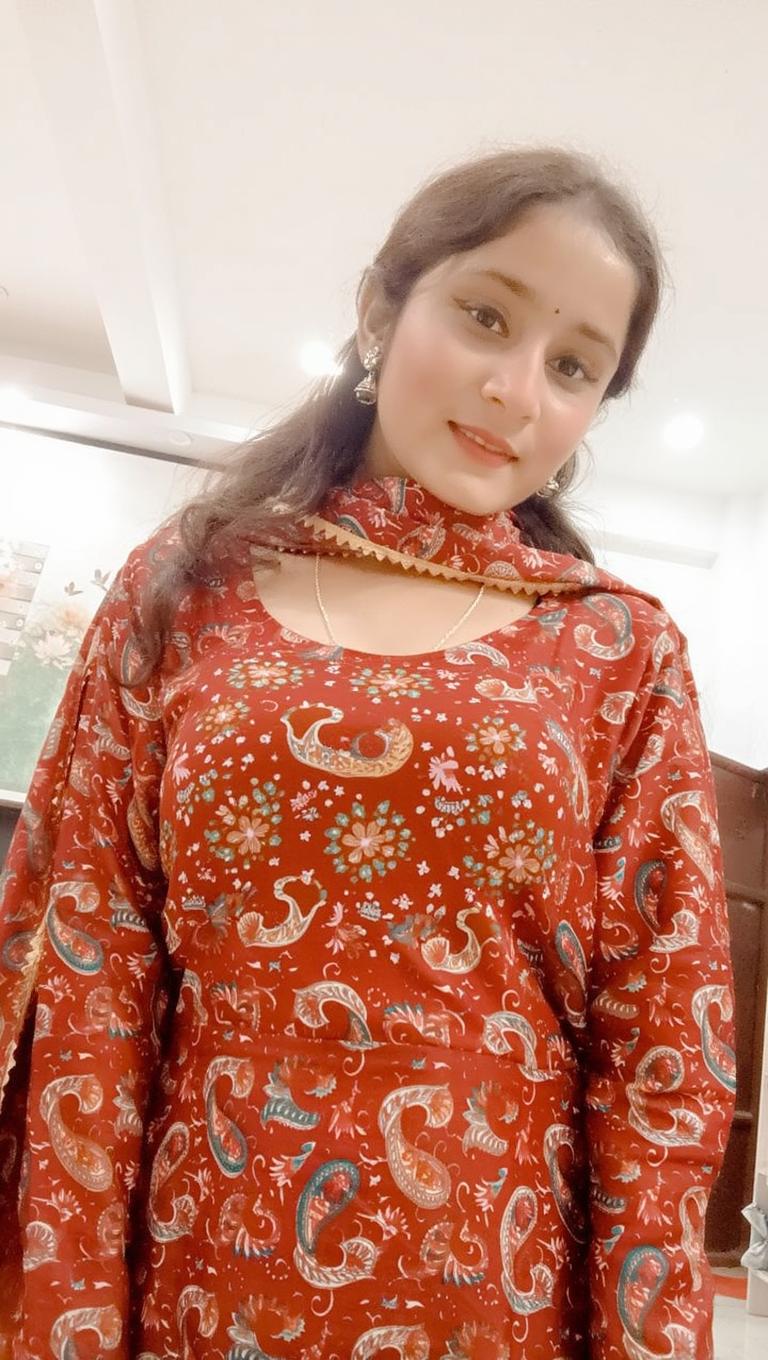 A young woman wearing a traditional red kurta with paisley patterns, smiling gently