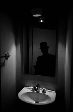 A spooky, eerie scene featuring a creepy shadow of a figure wearing a classic top hat, prominently reflected in a bathroom mirror