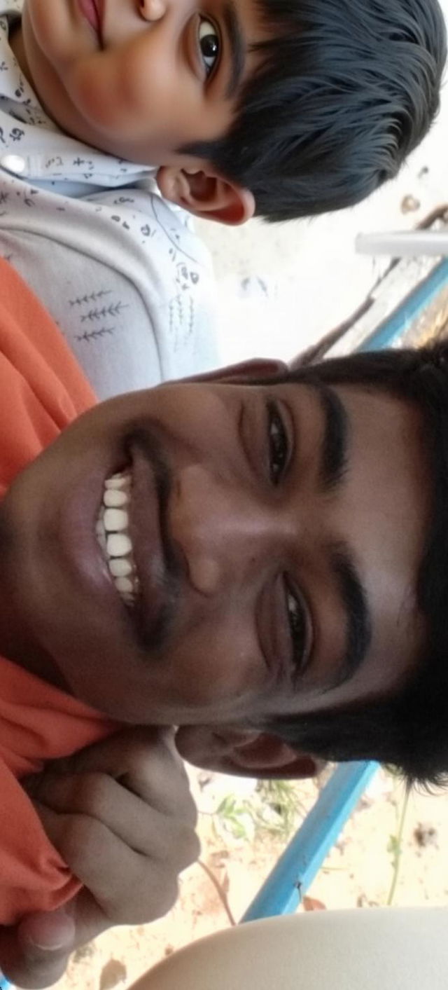 A joyful young man with a bright smile, medium brown skin, wearing an orange shirt