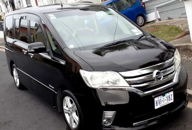 A sleek black van parked on a welcoming suburban street, showcasing its shiny exterior and modern design