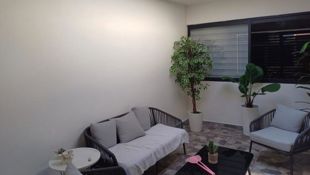 A cozy and modern indoor porch setting featuring a small round table with a plant, two stylish rattan chairs arranged with cushions, and a plush sofa with soft gray blankets