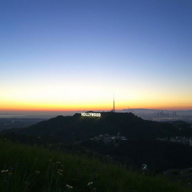 A stunning view of the Hollywood Sign at dusk, illuminated by the soft glow of the setting sun, with a clear sky transitioning from blue to orange and purple hues