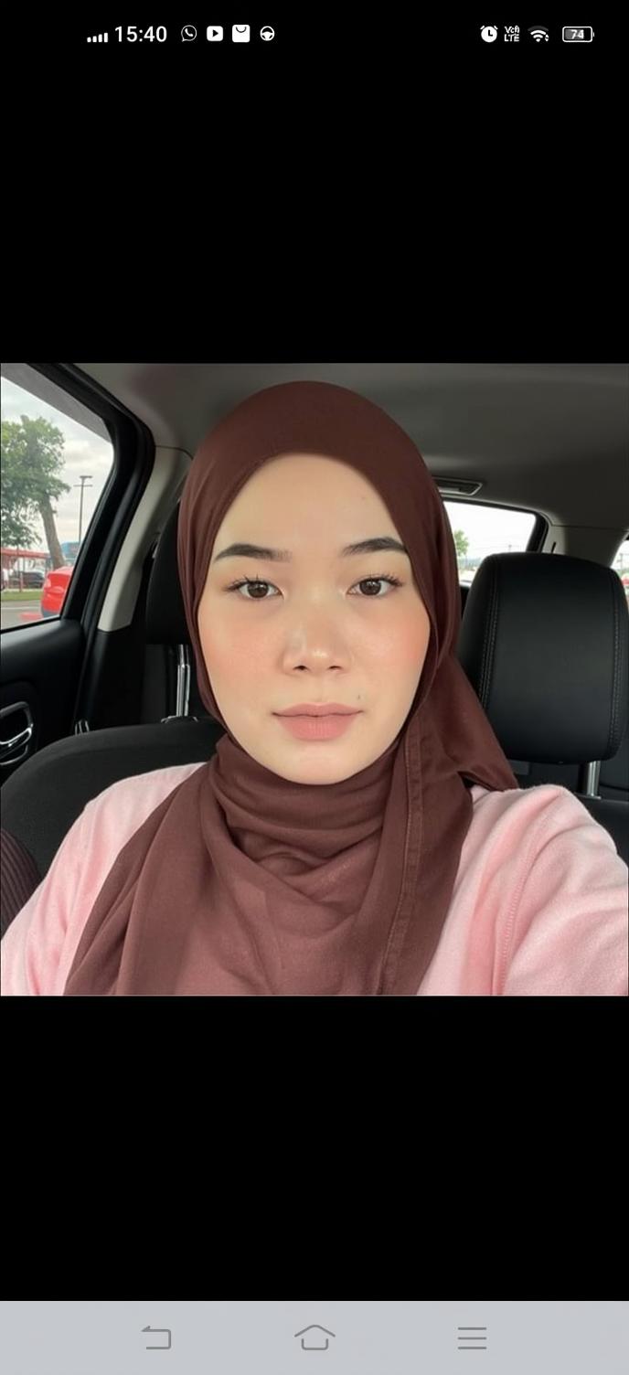 A portrait of a woman wearing a brown headscarf (hijab) and a light pink sweater, sitting in a car