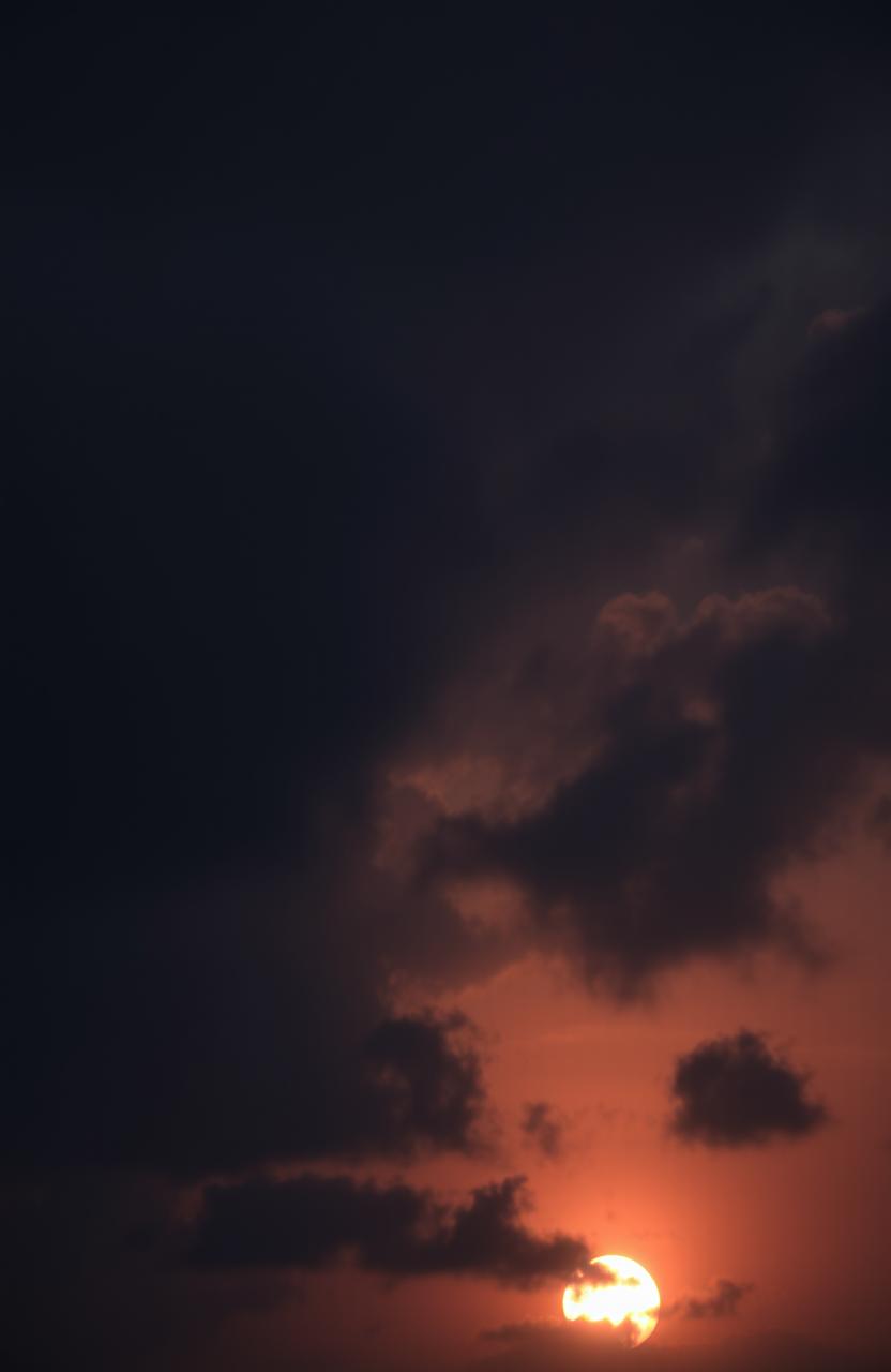 A dramatic sunset sky filled with dark, gloomy clouds, casting an ominous shadow over the horizon