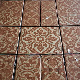 A close-up view of old vintage floor tiles, displaying intricate, faded patterns in earthy tones of brown, blue, and green