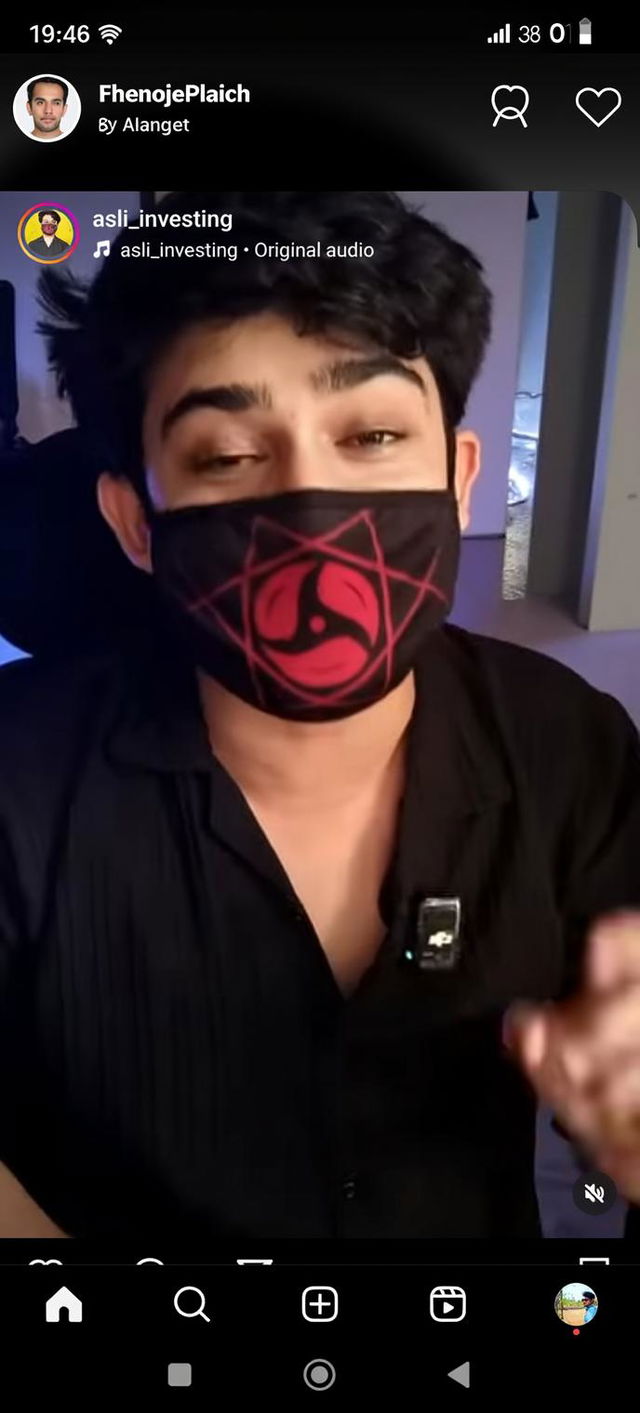 A close-up portrait of a young man wearing a stylish black shirt and a unique red and black mask with a geometric design