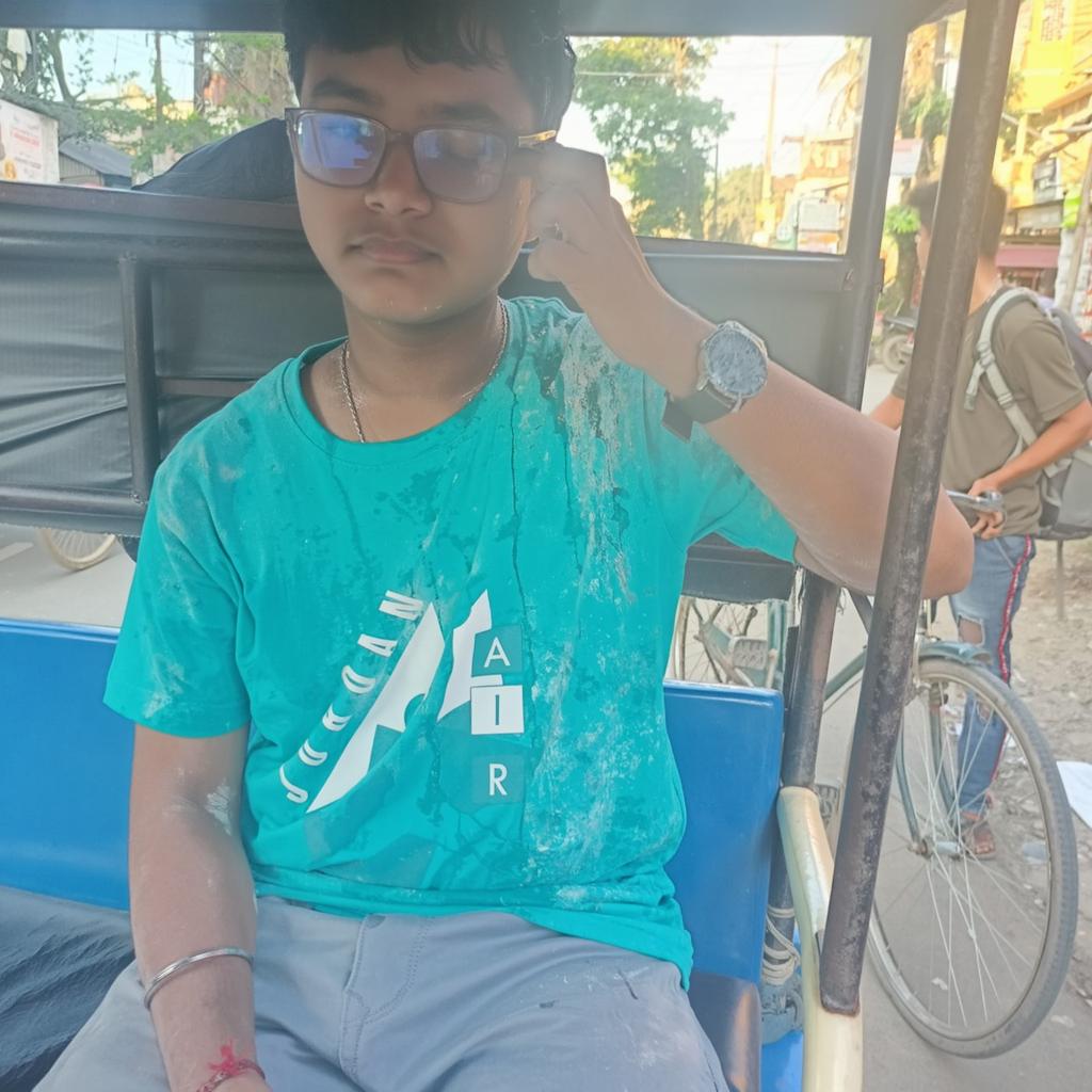 A young person sitting in a rickshaw, wearing a teal shirt with a bold logo and light gray pants