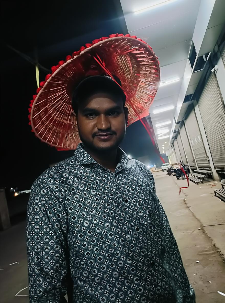 A man wearing a large, colorful straw hat standing in a dimly lit market street at night