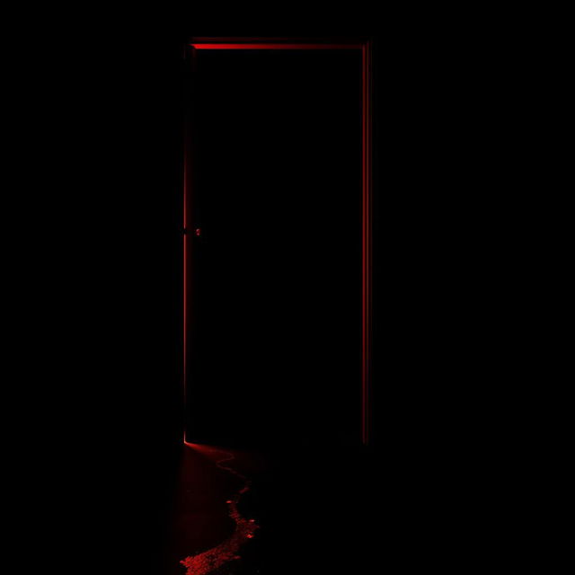 A black dark room featuring a slightly open door, with a vivid red light streaming out from the gap