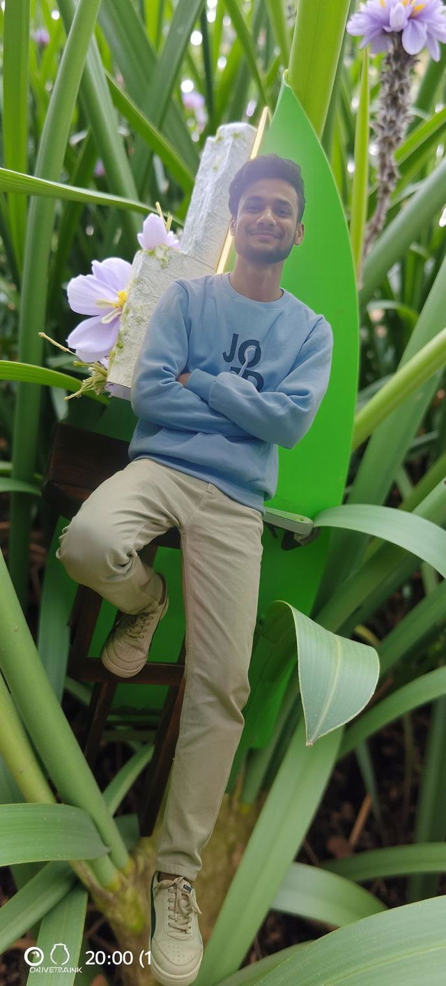 A young man standing casually against a bright green wall with a pizza restaurant logo in the background