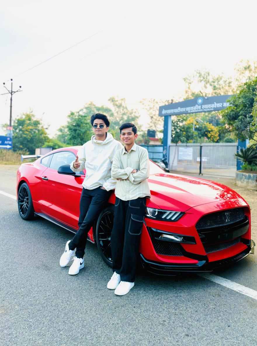 Two young men posing next to a striking red sports car on an open road