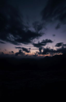 A mysterious dark landscape under a twilight sky, with swirling black clouds that suggest an ambiance of intrigue and depth