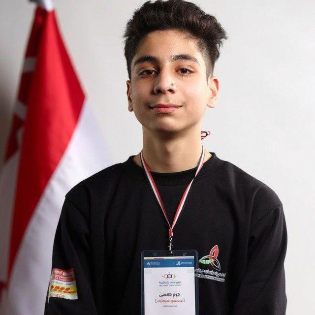 A young athlete wearing a black sweatshirt with a medal around his neck and a name tag, posing confidently against a light background