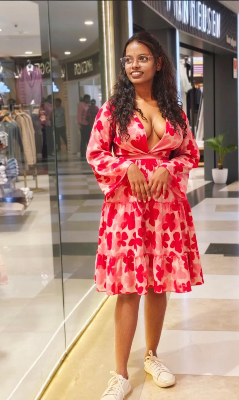 A young woman standing confidently in a vibrant floral dress with a deep neckline, set in a modern shopping mall with soft lighting and stylish interior design