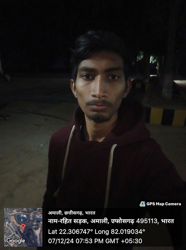 A young man standing in a dimly lit outdoor area, capturing a selfie at night