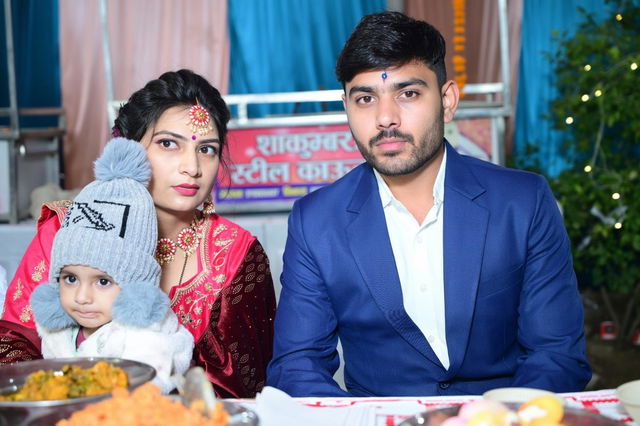 A close-up scene of a beautiful Indian wedding celebration, featuring a bride in a stunning red and gold lehenga with intricate traditional jewelry, sitting beside a groom in a smart blue suit