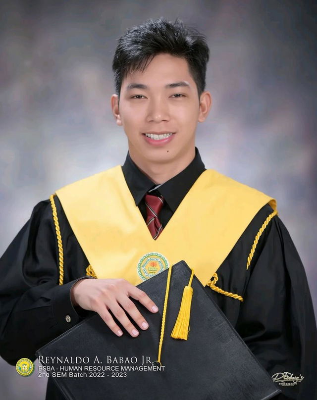 A young male graduate smiling proudly, wearing a black graduation gown and a bright yellow sash