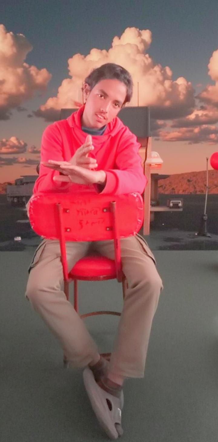 A young male programmer sitting in a vibrant red chair, with a serious expression, wearing a bright red hoodie and casual beige pants