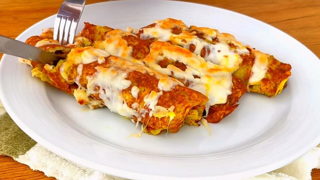 A beautifully plated dish of potato rolls, filled with seasoned mashed potatoes, wrapped in golden-brown tortillas, generously topped with melted cheese