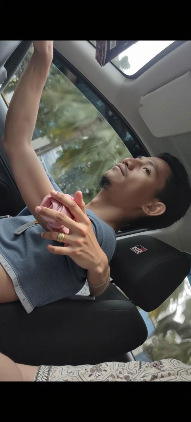 A relaxed young man sitting in the driver's seat of a modern car, wearing a casual gray t-shirt