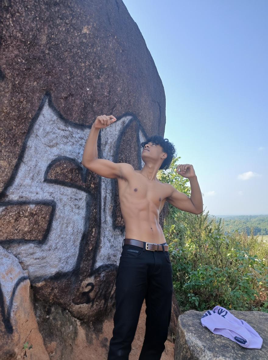 A fit young male with a defined six-pack abdomen, flexing his arms confidently in an outdoor setting