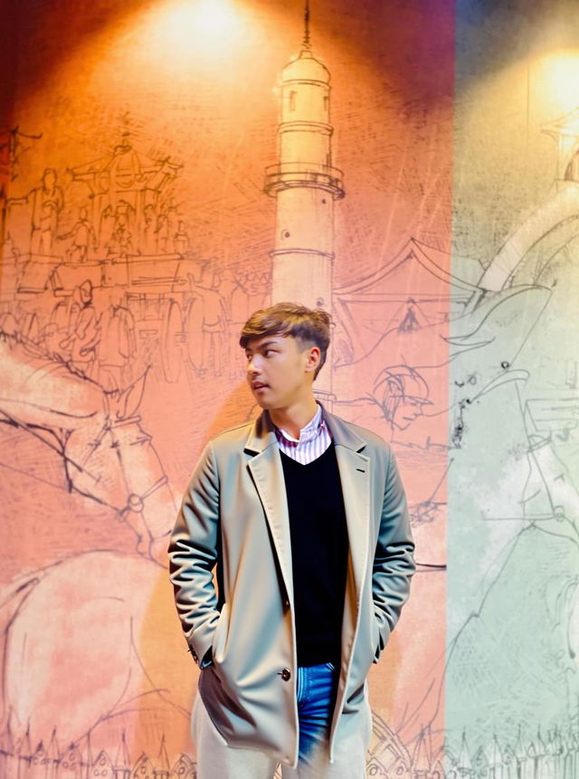 A young man in a stylish, silver bomber jacket stands confidently against a colorful mural background