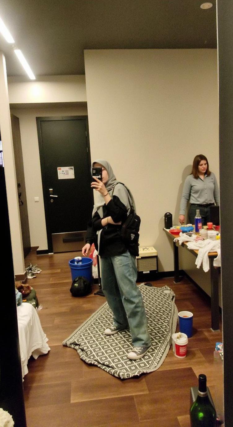 A stylish individual standing confidently in front of a mirror, dressed in casual wear with a black hoodie, loose jeans, and sneakers