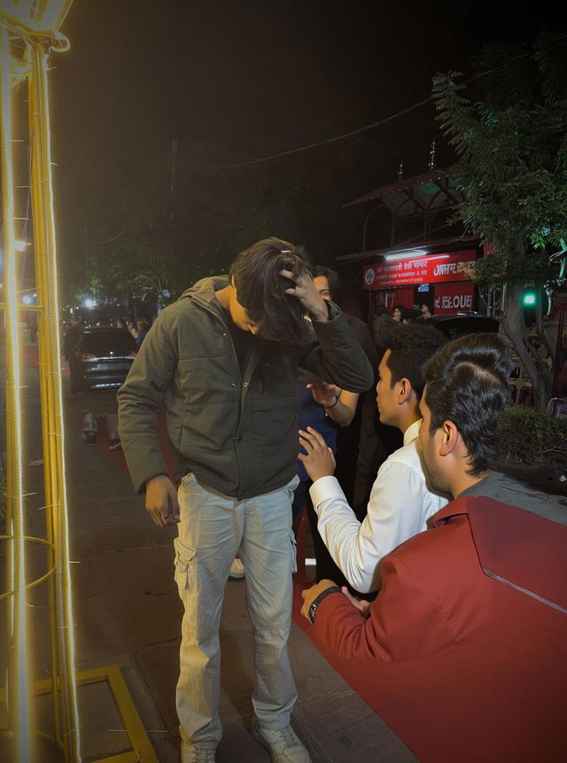 A solitary figure in a stylish green jacket and light-colored cargo pants, standing in the foreground against a softly illuminated street at night