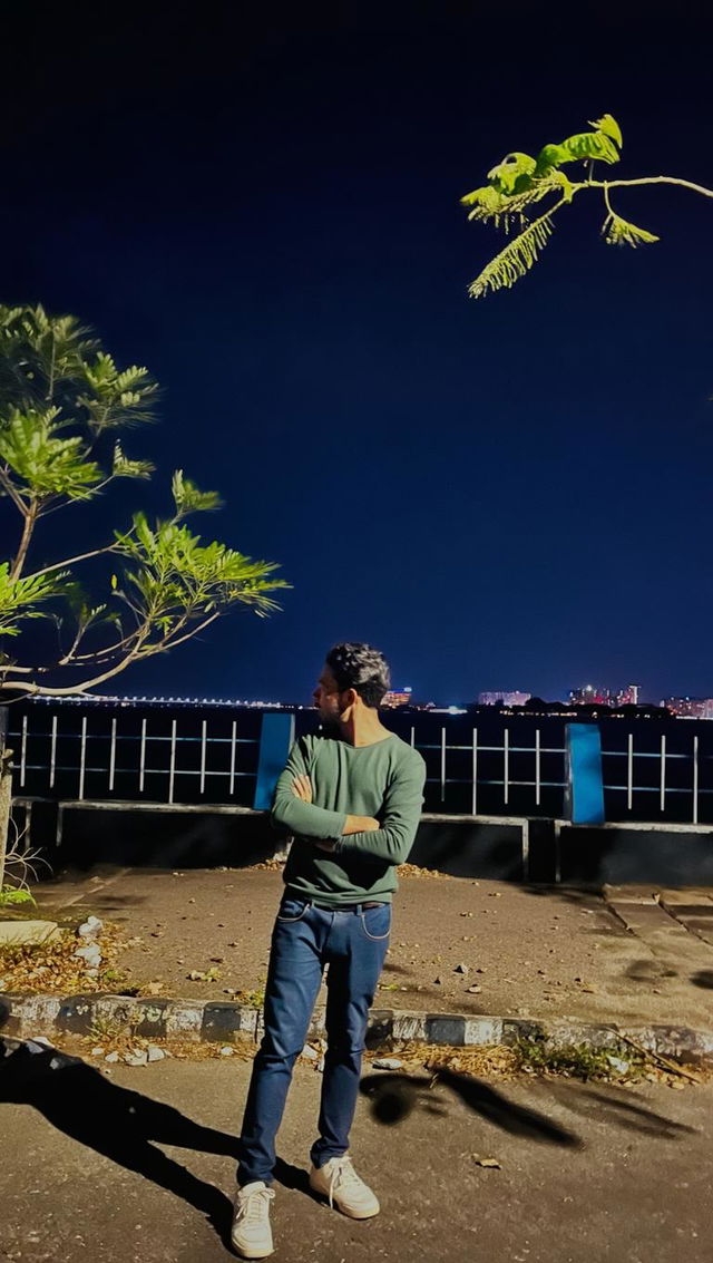 A stylish young man standing casually by a scenic waterfront at night