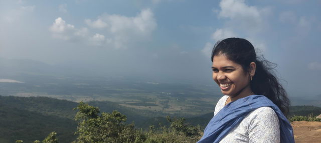 A scenic mountain view in a bright and cheerful atmosphere, showing a smiling woman with long, dark hair