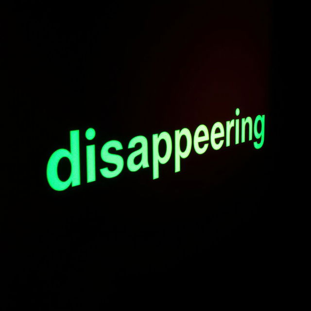 A dark room illuminated by a vivid xenon light that projects the word 'disappearing' onto the wall in bold, bright letters