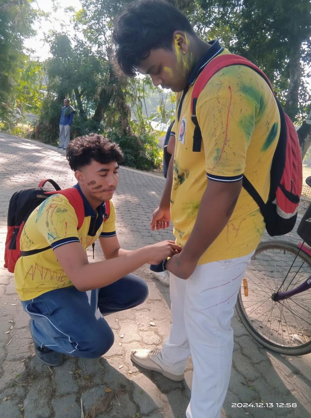 Two teenage boys having fun outdoors, one boy sitting down and playfully drawing on the shirt of the other boy, who is standing