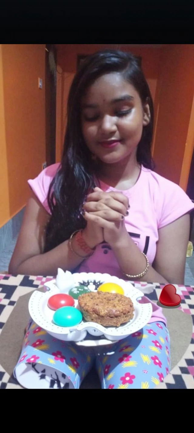 A young girl with long hair, wearing a pink T-shirt, sitting at a table with a colorful birthday cake in front of her