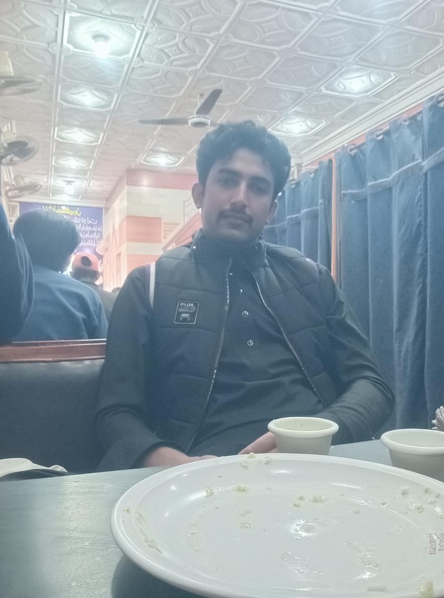 A cozy restaurant Setting with a young man in a stylish black vest sitting at a table