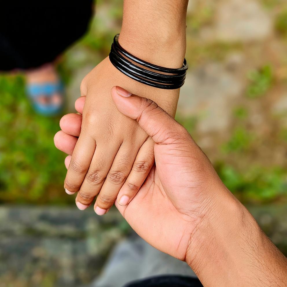 A close-up image of two hands holding each other, one adorned with black bangles