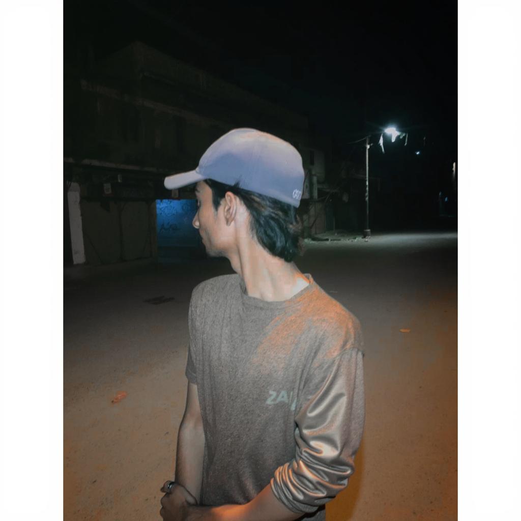 A young man with a hat, standing in a dimly lit street at night