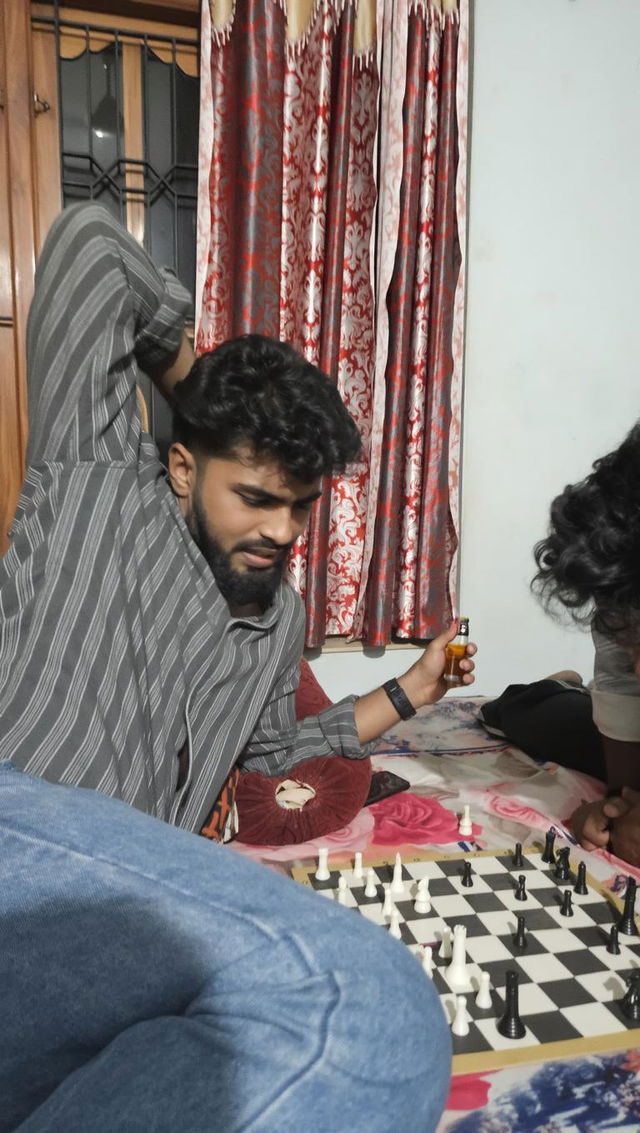 A young man sitting on a bed playing chess with a serious expression