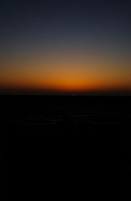 A silhouette of a woman sitting alone on a beach during sunset