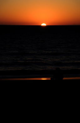 A silhouette of a woman sitting alone on a beach during sunset
