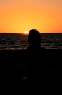 A silhouette of a woman sitting alone on a beach during sunset