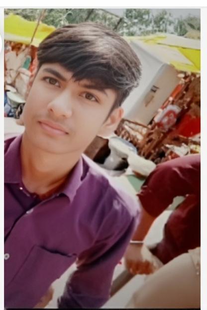 A young man with dark hair styled, wearing a purple shirt, standing in a lively outdoor market scene filled with colorful stalls and people in the background, bright sunlight filtering through the canopies above, capturing a friendly and approachable demeanor, with a slight smile on his face