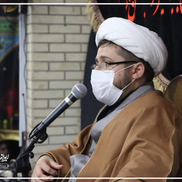 A scene depicting a religious figure with a turban and a face mask, passionately speaking into a microphone within the Imam Reza shrine