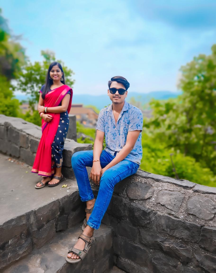 A young person sitting on a stone wall in an outdoor setting, wearing a blue floral shirt and stylish sunglasses