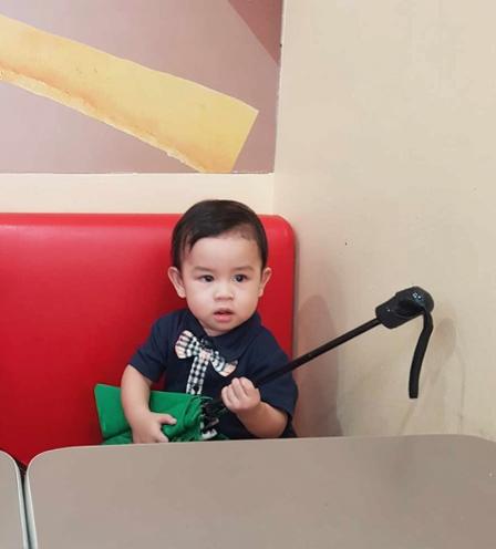 A cute young child sitting in a bright, colorful cafe, holding a green object in one hand and a music instrument resembling a guitar in the other