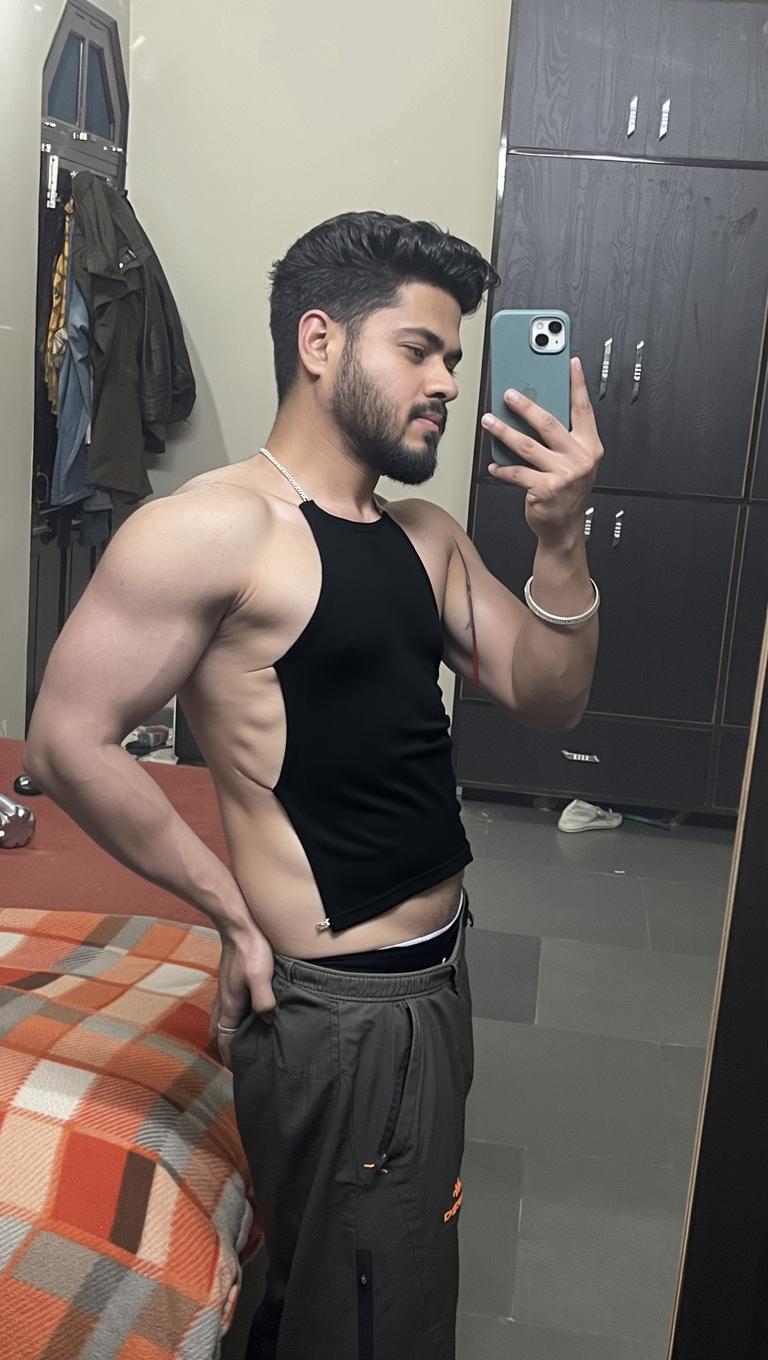 A young man posing in front of a mirror, wearing a sleeveless black shirt, showcasing a toned physique