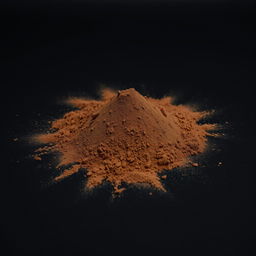 A mound of powder consisting of a gradient of black and brown shades, scattered on a plain, completely black background