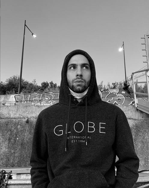 A young man standing confidently against a backdrop of urban graffiti at twilight